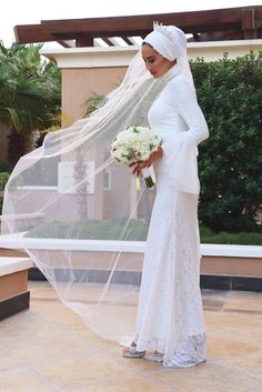 a woman in a wedding dress and veil standing on a patio with her hand under the veil