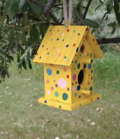 a yellow birdhouse hanging from a tree in the yard with polka dots on it