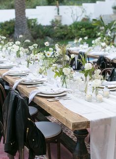 a long table is set with white flowers and place settings for an outdoor dinner party