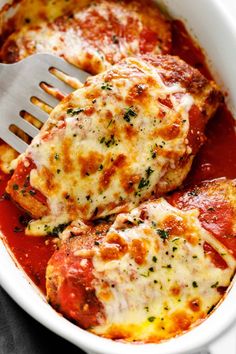 two pieces of chicken parmesan in a white casserole dish with a fork