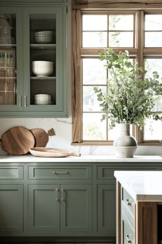 a kitchen with green cabinets and wooden cutting boards on the counter top, next to a window