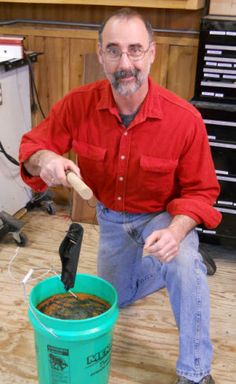 a man in a red shirt and jeans is pouring something into a green bucket