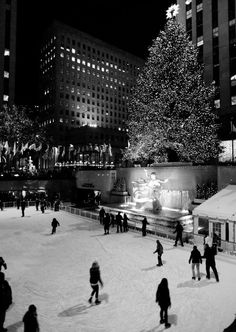 people skating on an ice rink in front of a large christmas tree with lit up lights