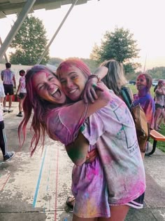 two girls hugging each other in front of a group of people covered in colored powder