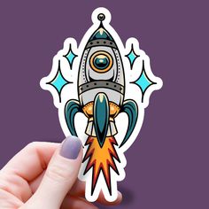 a hand holding up a sticker with a rocket ship on it