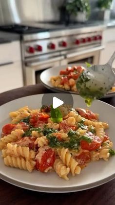 a white plate topped with pasta covered in tomato sauce and greens next to an oven