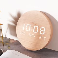 an alarm clock sitting on top of a table next to a book and vase with flowers