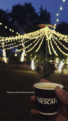 a hand holding a cup of coffee with lights in the background