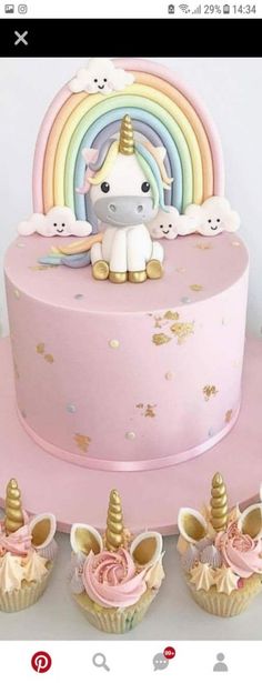 there is a pink cake with unicorns on it and cupcakes next to it