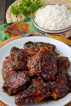 a white plate topped with meat and rice next to a bowl filled with rice on top of a wooden table