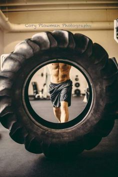 a shirtless man standing in front of a large tire with his legs spread out