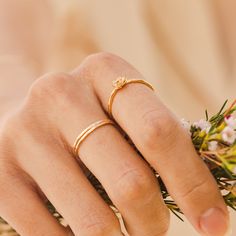 a close up of a person's hand with two rings on their fingers and flowers in the background