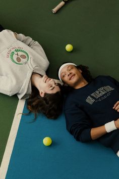 two people laying on the ground with tennis balls