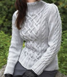 a woman sitting on top of a rock wearing black gloves and a white knitted sweater