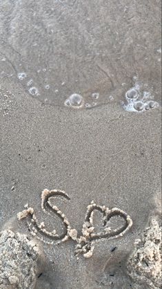 the word love is written in the sand at the beach with two hearts drawn on it