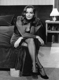 a woman sitting on top of a bed next to a night stand with a lamp