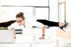 two women in business attire are on their laptops and one is doing a handstand