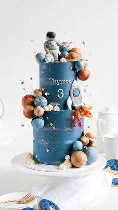 a three tiered blue cake with stars and planets on it's side, sitting on a white plate