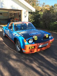 an orange and blue race car parked in front of a garage with its hood up