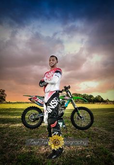 a man standing next to a dirt bike on top of a grass covered field under a cloudy sky