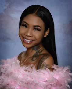 a woman with tattoos and pink feathers on her chest smiling at the camera while posing for a photo