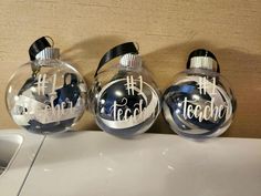 three christmas ornaments are sitting on a counter top, one has the word teach written on it