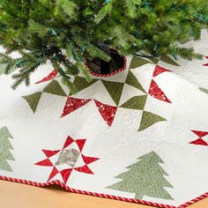 a quilted christmas tree skirt with red and green stars on it, sitting next to a pine tree