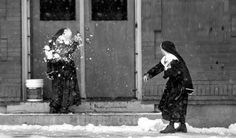 two women are standing in front of a building with snow on the ground and one is throwing flowers into the air