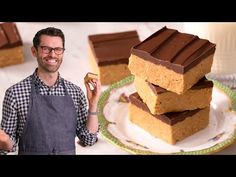 a man holding a piece of cake next to a stack of brownies on a plate