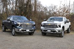 two pickup trucks parked next to each other on a gravel road in front of trees