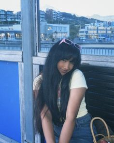 a woman with long black hair sitting on a bench next to a bag and purse