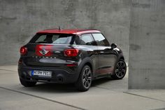 the rear end of a small car parked in front of a concrete wall with graffiti on it