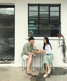 a man and woman sitting at a table talking to each other in front of a building