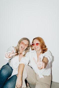 two women sitting on the floor with their hands in the air and pointing at something