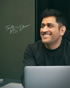 a man sitting at a desk with a laptop computer in front of him and writing on the wall behind him