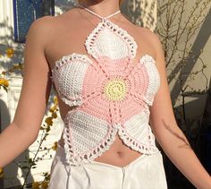 a woman wearing a pink crochet top and white pants with flowers on it