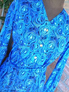 "Gorgeous vintage pre-loved dress from the 60's Bright colors on several blue tone, turquoise, celeste, skyblue Golden buttons with KS logo, long sleeves with 1 golden button, skinny belt made with the same fabric. Great vintage condition, no visible defects, pre-loved MATERIAL label says Ban-Lon (an hight quality nylon, silk touch) BRAND Ken Scott SIZE small/ M Vintage 10 (please refers on measures above) Approx measures taken flat shoulder cm 36 chest cm 43 Waist line cm 42 Hipsline cm 49 hem Blue Fitted Dress With Abstract Print, Vintage Blue Printed Dress, Blue Retro Dress With Vintage Print, Fitted Blue Dress With Bold Print, Blue Vintage Dress With Vintage Print, Blue Retro Dress With Retro Print, Bohemian Blue Dress With Graphic Print, 1970s Blue Fitted Dress, 1970s Blue Long Sleeve Dress