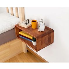 a small wooden table with some books and cups on it next to a white bed