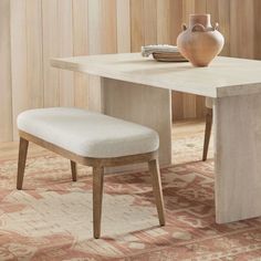 a dining table with a bench and vase on the top, in front of a wooden paneled wall