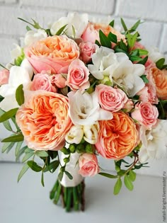 a bridal bouquet with peach and white flowers in front of a brick wall on a table