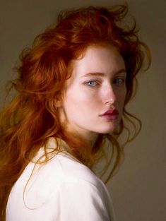 a woman with red hair and blue eyes is posing for the camera while wearing a white shirt