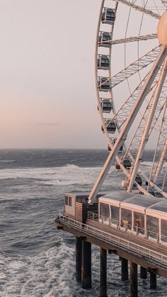 a ferris wheel sitting on top of a pier next to the ocean with waves coming in