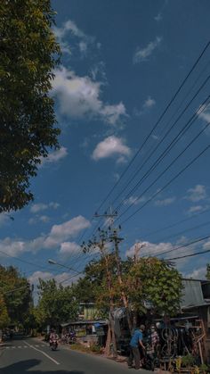 people are standing on the side of the road near power lines and telephone poles, under a blue sky with white clouds