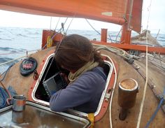 a woman sitting on the back of a boat using a cell phone and drinking coffee