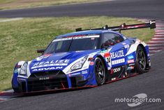 a blue nissan sports car driving on a race track with grass and bushes in the background