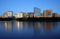 the city skyline is reflected in the still water of the lake at twilight, with skyscrapers and trees on either side