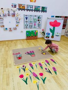 a child is playing with flowers on the floor in front of a wall full of pictures