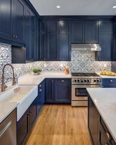 a kitchen with dark blue cabinets and white counter tops, wood flooring and stainless steel appliances