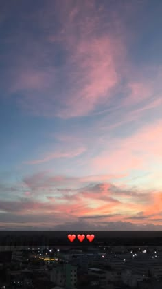 two heart shaped balloons floating in the air at sunset or dawn over a cityscape