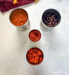 four small metal cups filled with different types of beans and sauces on top of a table